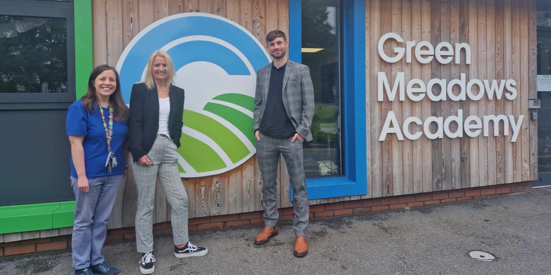 News page: Green Meadows Academy teaching staff member, Caren and Callum standing outside the school building
