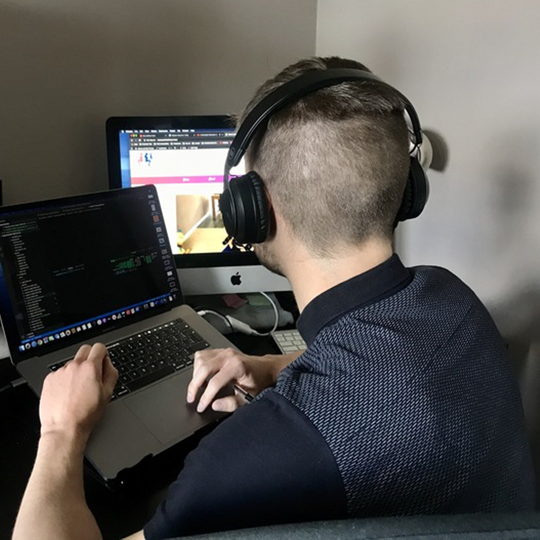 Our return to website accessibility image: Callum is sat down with his headphones on. He is working with a dual-screen setup. The first screen is his laptop to the left. The second is a bigger computer monitor on the right.